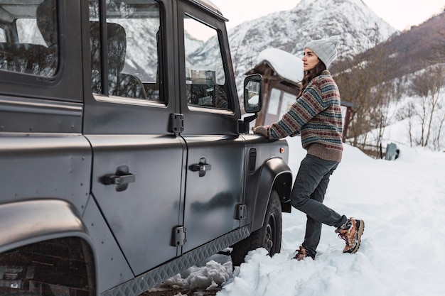 Jong meisje dat de besneeuwde berg bekijkt die tegen haar auto in de Italiaanse Alpen leunt.