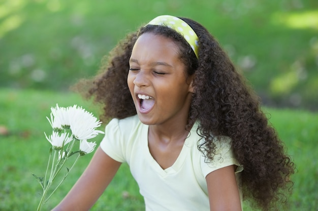 Jong meisje dat een bloem houdt en in het park niest