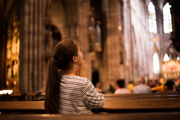 Jong meisje dat in kerk bidt die zich op haar knieën bevindt