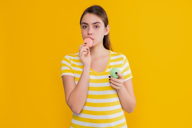 Jong meisje dat macaron op gele achtergrond eet