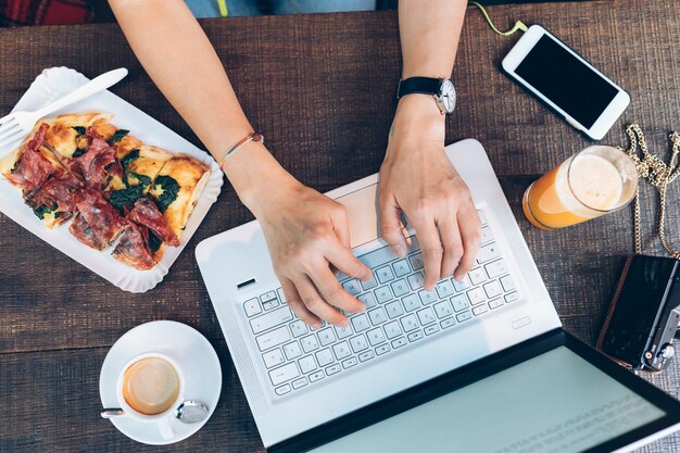 Jong meisje dat met laptop werkt terwijl het eten van pizza