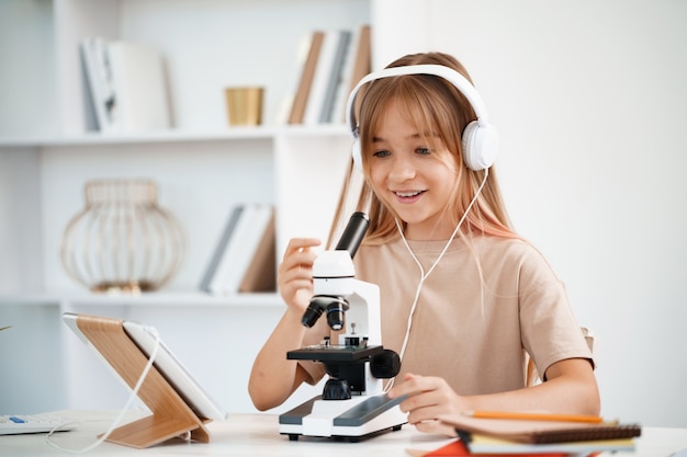 Jong meisje dat microscoop gebruikt tijdens online lesonderwijs thuis