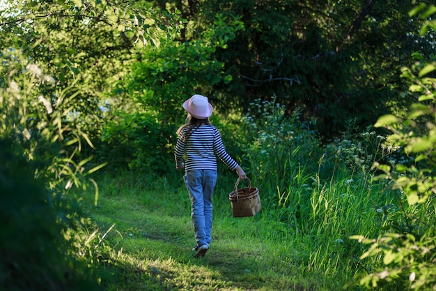 Jong meisje dat op een weg door groene bossen loopt die een mand birchbark draagt