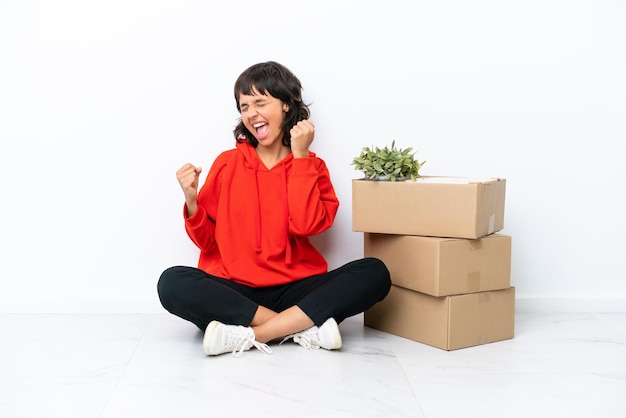 Jong meisje dat zich in nieuw huis tussen dozen beweegt die op witte achtergrond worden geïsoleerd en een overwinning viert