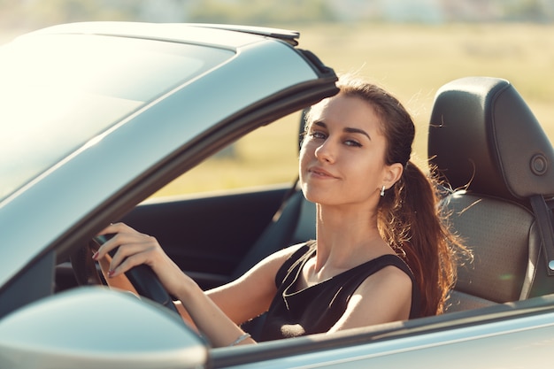 Jong meisje die cabrioauto drijven, op zonsonderganglicht