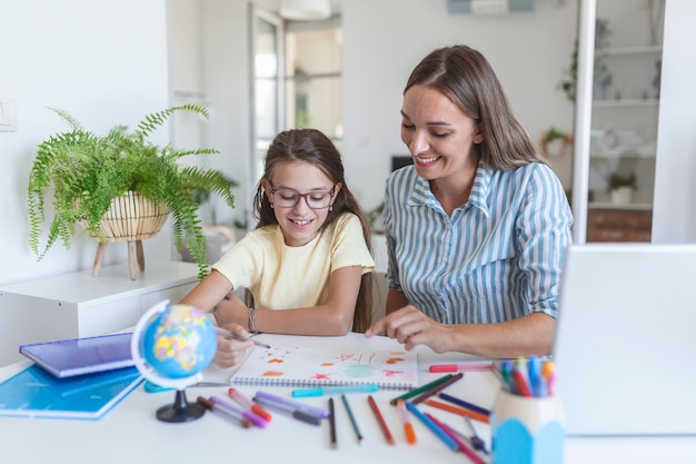 Jong meisje doet haar school huiswerk met haar moeder, thuis, ze schrijft op een boek. Moeder en kinddochter die thuis huiswerk schrijven en lezen