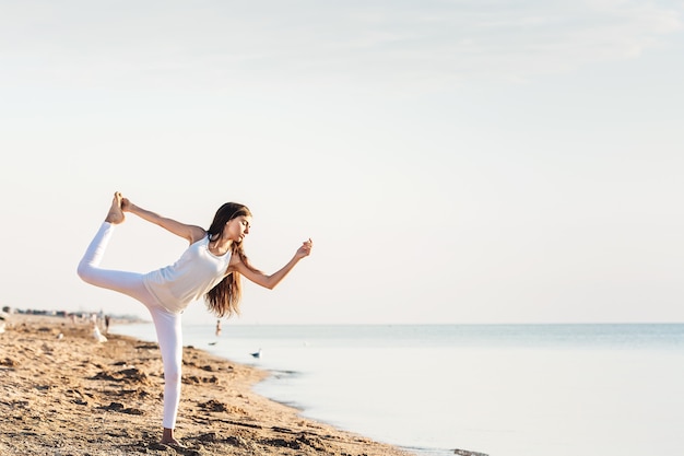 Jong meisje doet yoga bij zonsopgang op het strand.