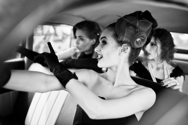 Jong meisje drie in retro stijl kleden stoel op oude klassieke vintage auto en plezier emoties
