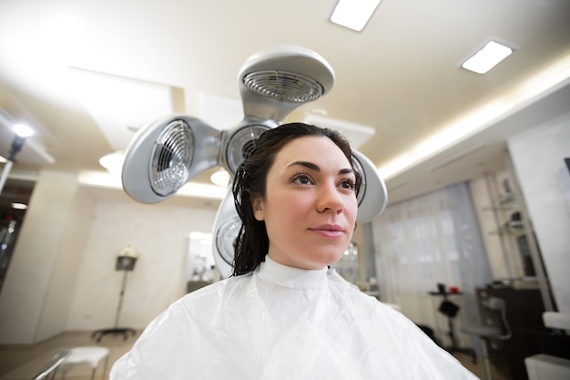 Jong meisje droogt haar haren in een kapper met een professionele föhn. portret van een jonge vrouw in een kapper