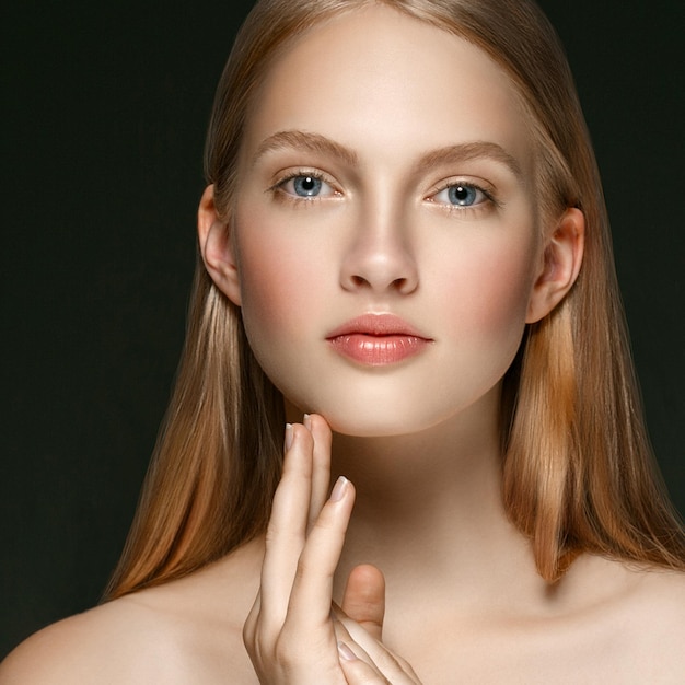 Jong meisje gezicht schoonheid huid portret met lang blond haar met hand over donkere achtergrond. Studio opname.