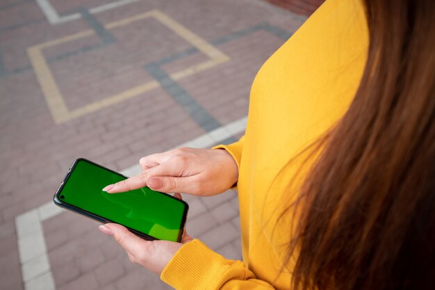 Jong meisje in een gele trui houdt een smartphone op straat