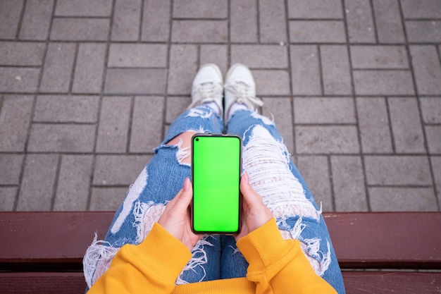 Jong meisje in een gele trui houdt een telefoon met een groen scherm op haar knieën