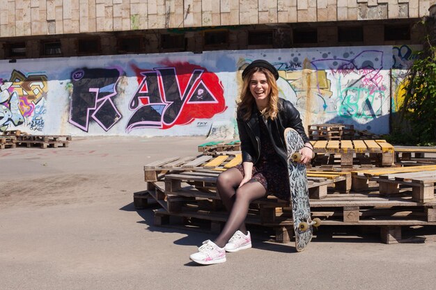 Foto jong meisje in een hoed zittend met het skateboard en lachen