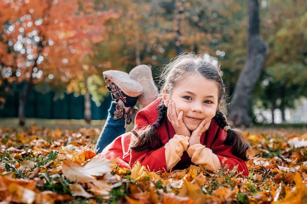 Jong meisje in een rode jas ligt op het gras en bladeren in een herfstpark