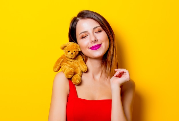 Jong meisje in een rode jurk met teddybeerstuk speelgoed op haar gele schouder