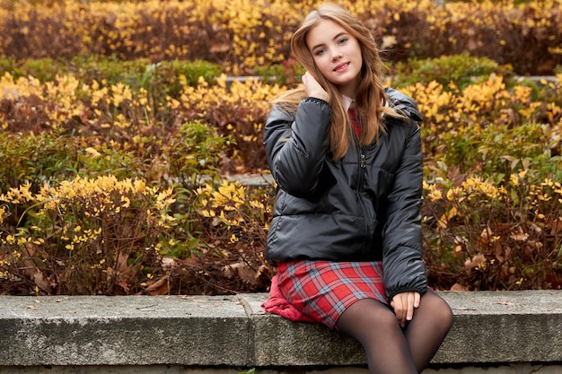 Jong meisje in een rode rok zit in het park in de herfst