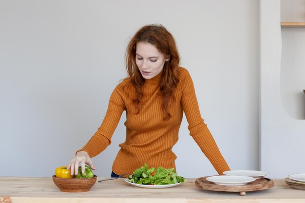 Jong meisje in een schort maakt een gezonde salade van groenten en kruiden in haar keuken