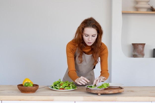 Jong meisje in een schort maakt een gezonde salade van groenten en kruiden in haar keuken