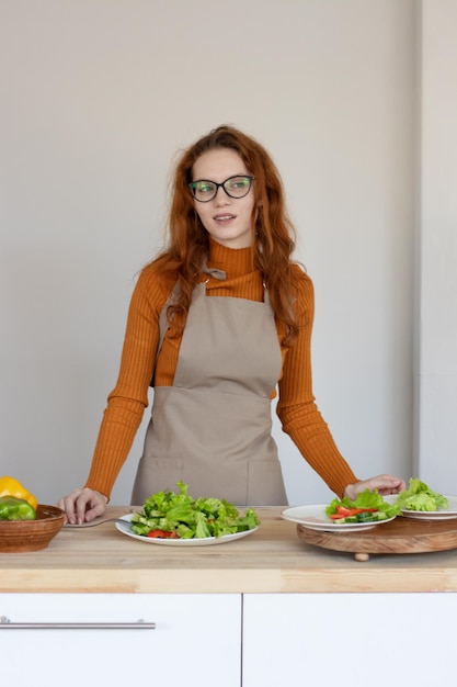 Jong meisje in een schort maakt een gezonde salade van groenten en kruiden in haar keuken