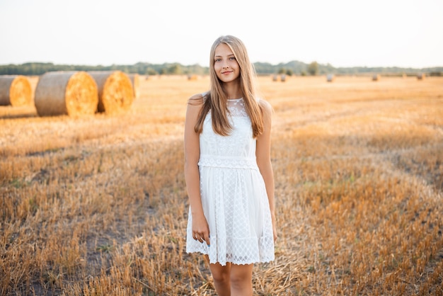 Jong meisje in een witte jurk op het gebied van geoogste rogge. Portret van een vrolijk meisje in het veld