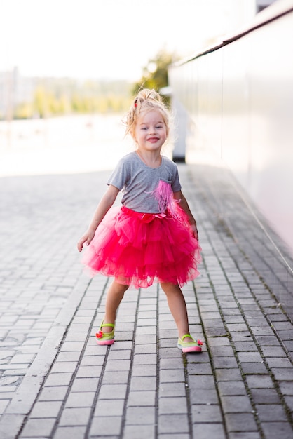 Jong meisje in elegante roze rok die op treden loopt