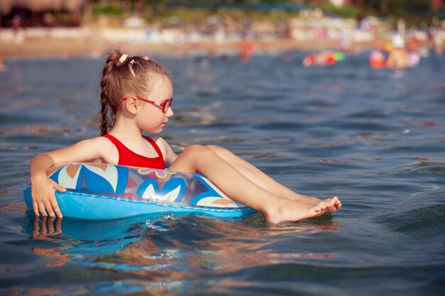 Jong meisje in glazen speelt in het water op een opblaasbare donut in een hete zonnige zomer