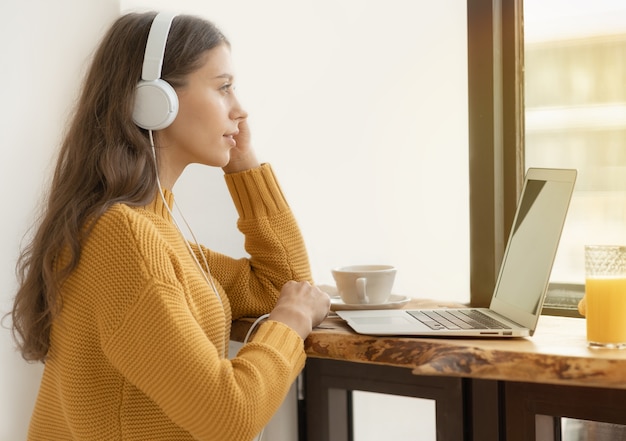 Jong meisje in hoofdtelefoons die online studeren, laptop gebruiken en ontbijten