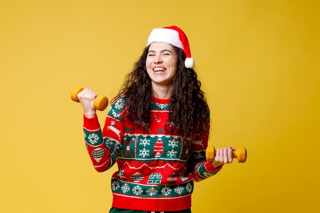 jong meisje in kerstkleding en kerstmuts traint fitness op gele geïsoleerde achtergrond