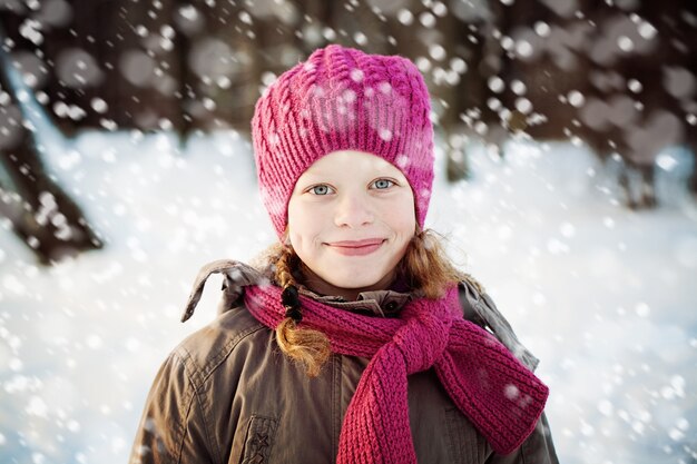 Foto jong meisje in roze muts en sjaal in park in besneeuwde winterdag. kind meisje buitenshuis