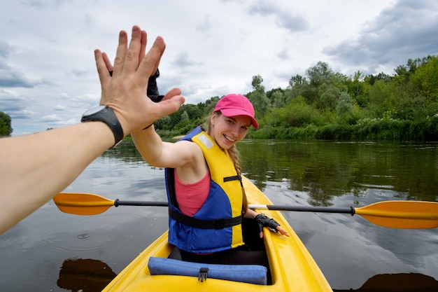 Jong meisje in roze pet roeien in kajak over de rivier, geven high five aan haar teamgenoot