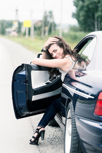 Jong meisje in speelse poses in jeans en een T-shirt glimlachend poserend in een auto aan de kant van de snelweg