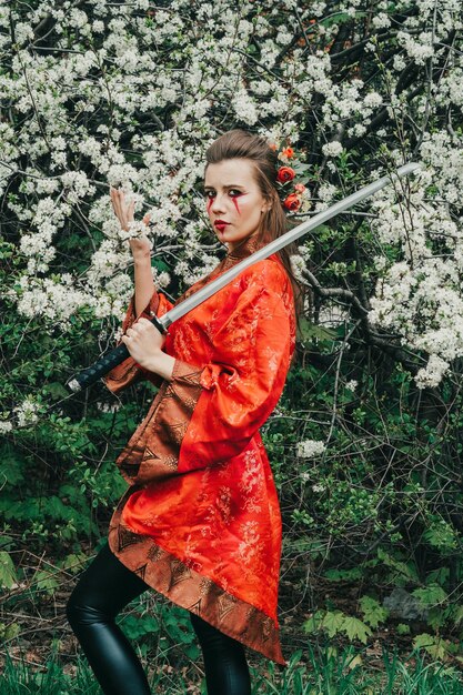 Jong meisje in traditionele kimano in een bloeiende tuin met samoerai Japanse zwaard katana in beeld van krijger vrouw