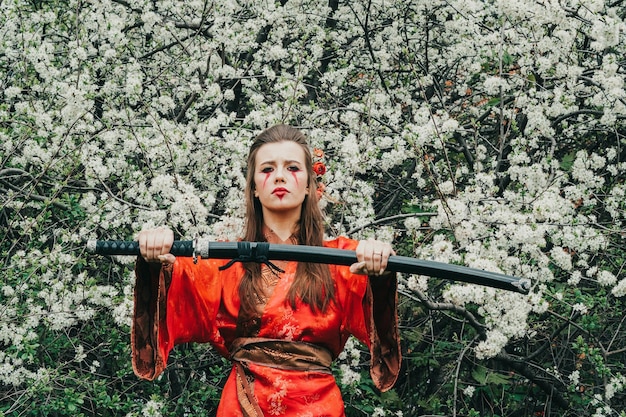 Jong meisje in traditionele kimano in een bloeiende tuin met samoerai Japanse zwaard katana in beeld van krijger vrouw