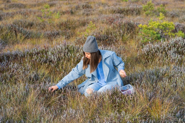 Jong meisje in trendy kleding die veenbessen plukt en geniet van zonnig herfstweer op het platteland