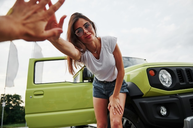 Jong meisje in zomerkleren, blij je te zien. Groene auto achter.