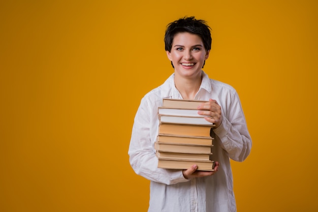 jong meisje lacht en houdt veel boeken op een gele achtergrond