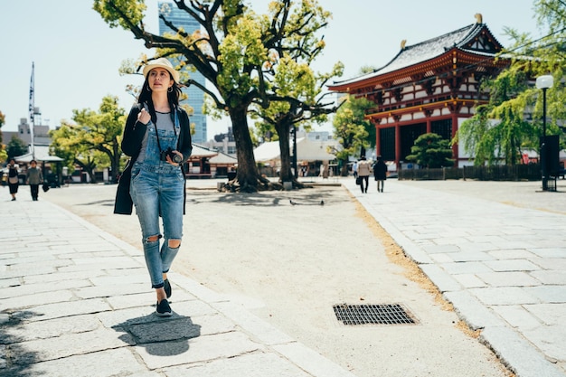 jong meisje lens man lopen buiten de tempel op zonnige dag in de zomervakantie. chinese vrouwelijke fotograaf die in osaka japan reist. zelfgeleide reis in jp lifestyle-concept.