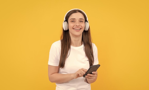 Jong meisje luistert muziek in hoofdtelefoons houdt telefoon op gele achtergrondtechnologie