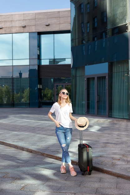 Jong meisje met bagage in de zomer in de buurt van het gebouw