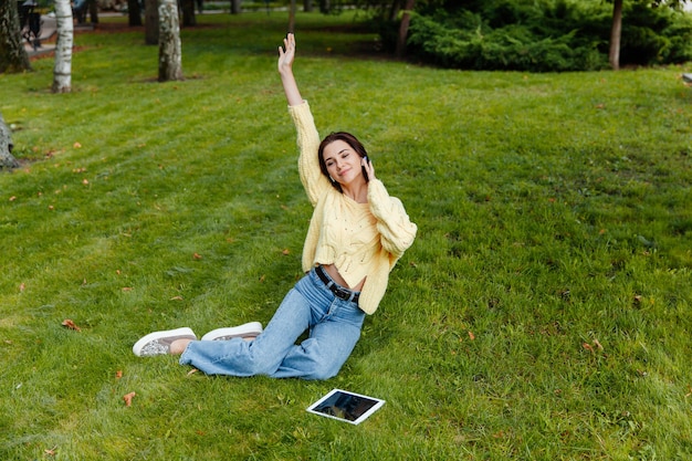 Jong meisje met behulp van een smartphone en koptelefoon, luisteren naar muziek in het park, buiten, zittend op het gras.