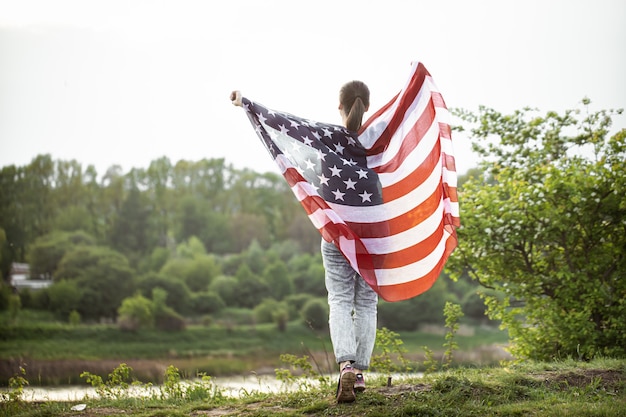 Jong meisje met de vlag van Amerika in de natuur vanaf de achterkant.