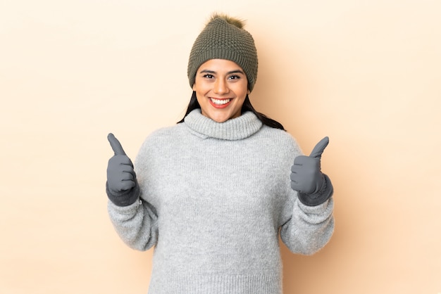 Jong meisje met de winterhoed op het beige muur geven duimen omhoog gebaar