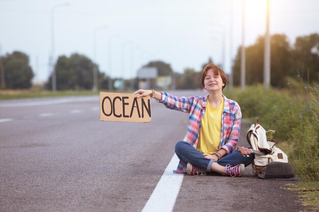 Jong meisje met een gitaar die langs de weg komt en aan het liften is