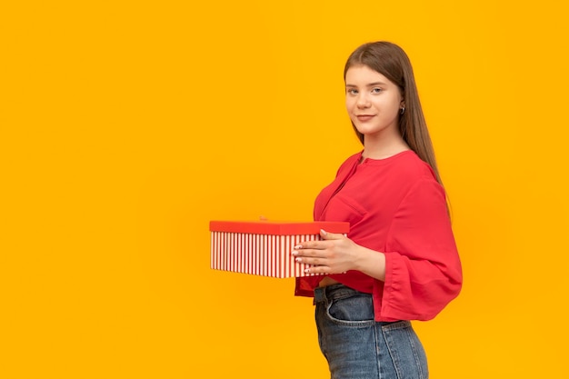 Jong meisje met geschenkdoos in haar handen op gele achtergrond Glimlachende tiener met geschenk op oranje achtergrond