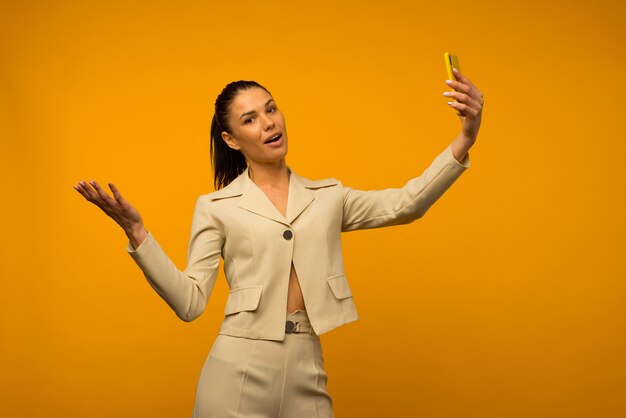 Jong meisje met huidproblemen van het gezicht poseren met een smartphone op een gele achtergrond.