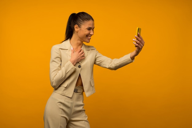 Jong meisje met huidproblemen van het gezicht poseren met een smartphone op een gele achtergrond.