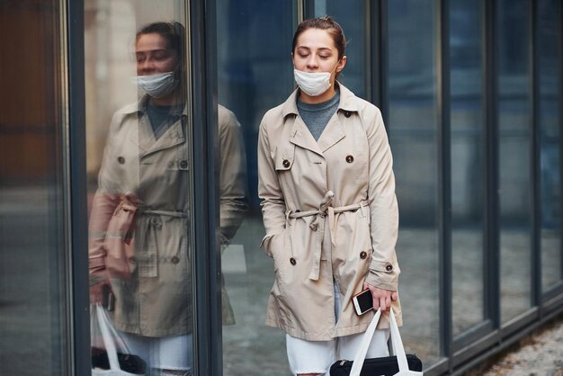 Jong meisje met jas en wit beschermend masker dat buiten in de buurt van het gebouw staat