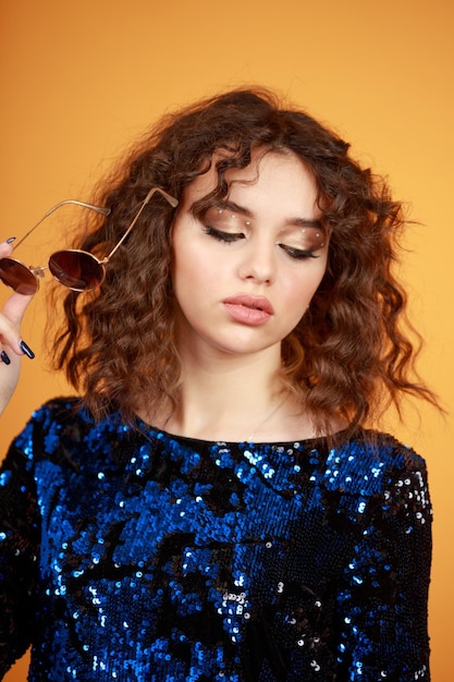 Jong meisje met krullend haar op een oranje achtergrond die haar zonnebril afdoet Foto van hoge kwaliteit