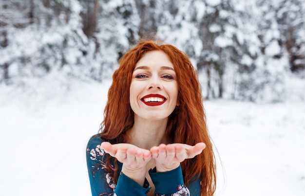 Jong meisje met lang rood haar in een zomerjurk op een winterlandschap. Een kus blazen