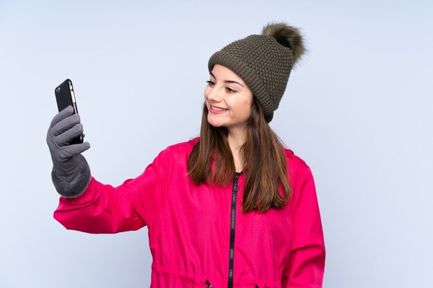 Jong meisje met muts op blauwe muur maken van een selfie